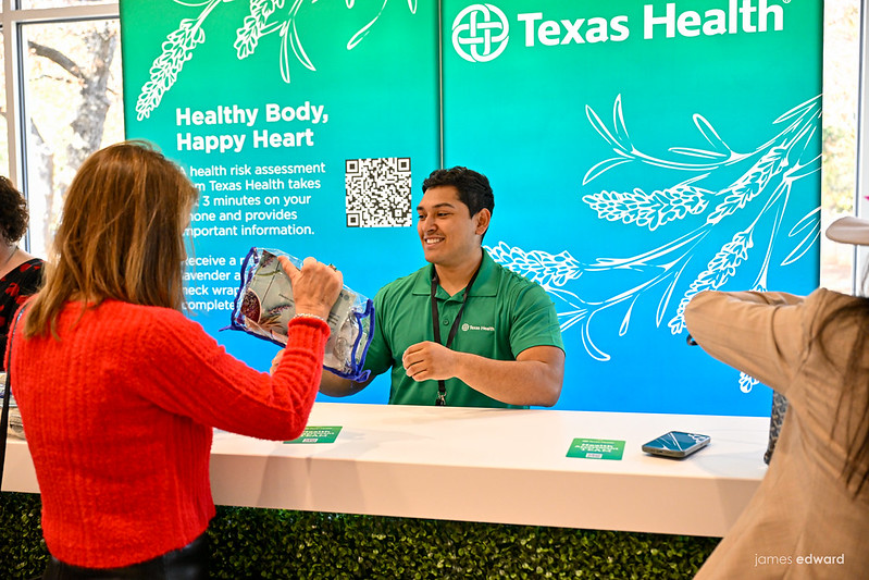 Woman in red accepting goody bag from man at Texas Health vendor booth